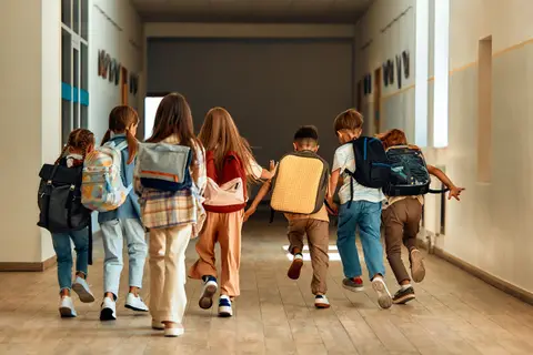 Enfants vus de dos, cartables sur le dos, courant dans un couloir d'école