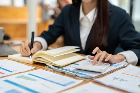 Femme calculant un budget avec une calculatrice et un carnet devant des documents chiffrés