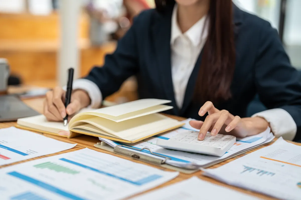 Femme calculant un budget avec une calculatrice et un carnet devant des documents chiffrés