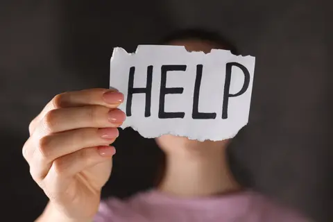 Personne tenant devant son visage un papier sur lequel est écrit « HELP »