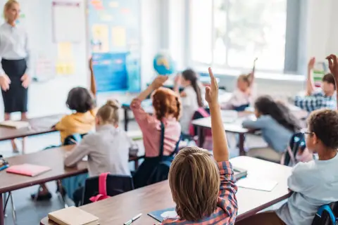 Élèves levant la main en classe face à leur enseignante