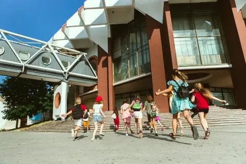 Groupe d'enfants avec leurs sacs à dos courant vers l'entrée d'un grand bâtiment scolaire sous le soleil