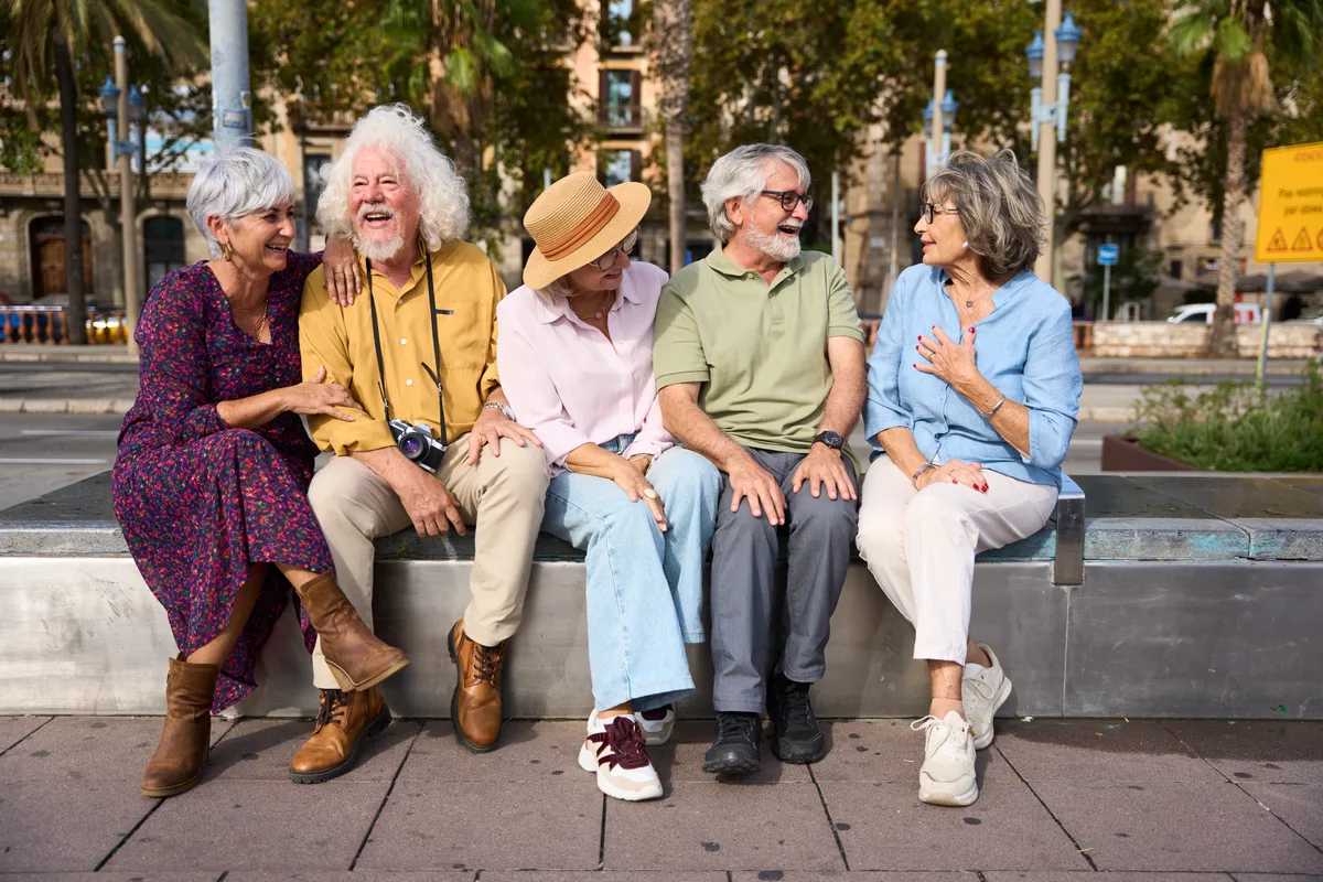 Groupe de retraités souriants assis sur un banc dans une rue de centre-ville