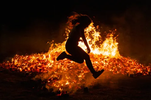 Silhouette d'une personne sautant par-dessus les braises d'un feu de joie, tradition de la nuit de la Saint-Jean