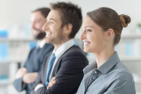 Trois professionnels souriants côte à côte dans un bureau