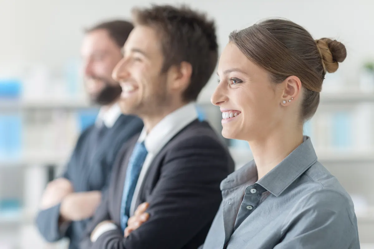 Trois professionnels souriants côte à côte dans un bureau